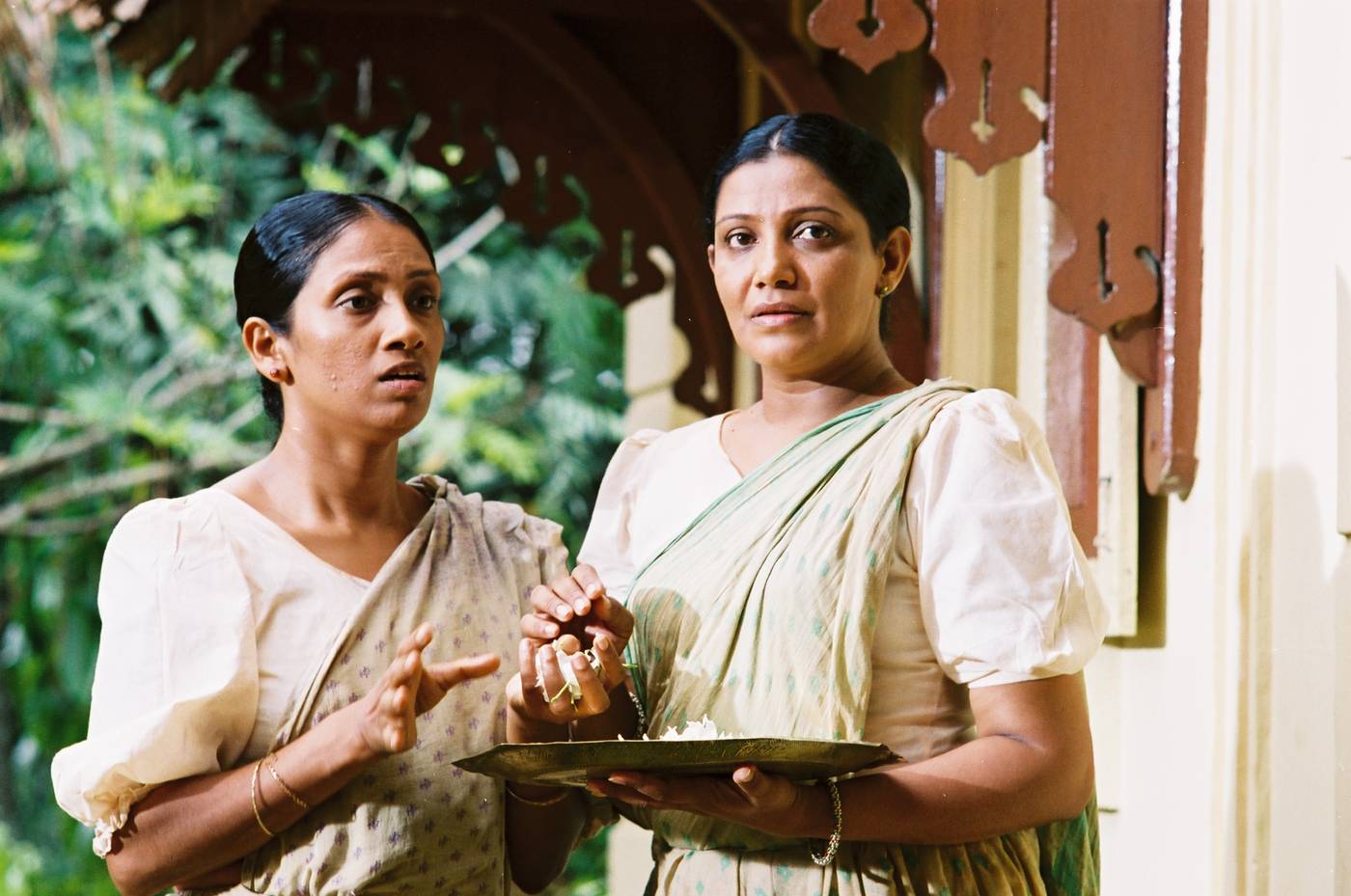 Two women on a verandah holding a brass tray of flowers